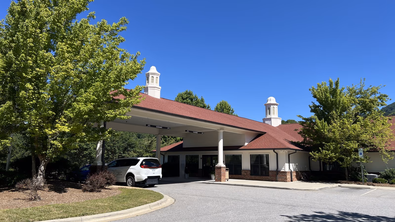Senior living facility with a red roof, brick accents, and a covered porte-cochère entrance.