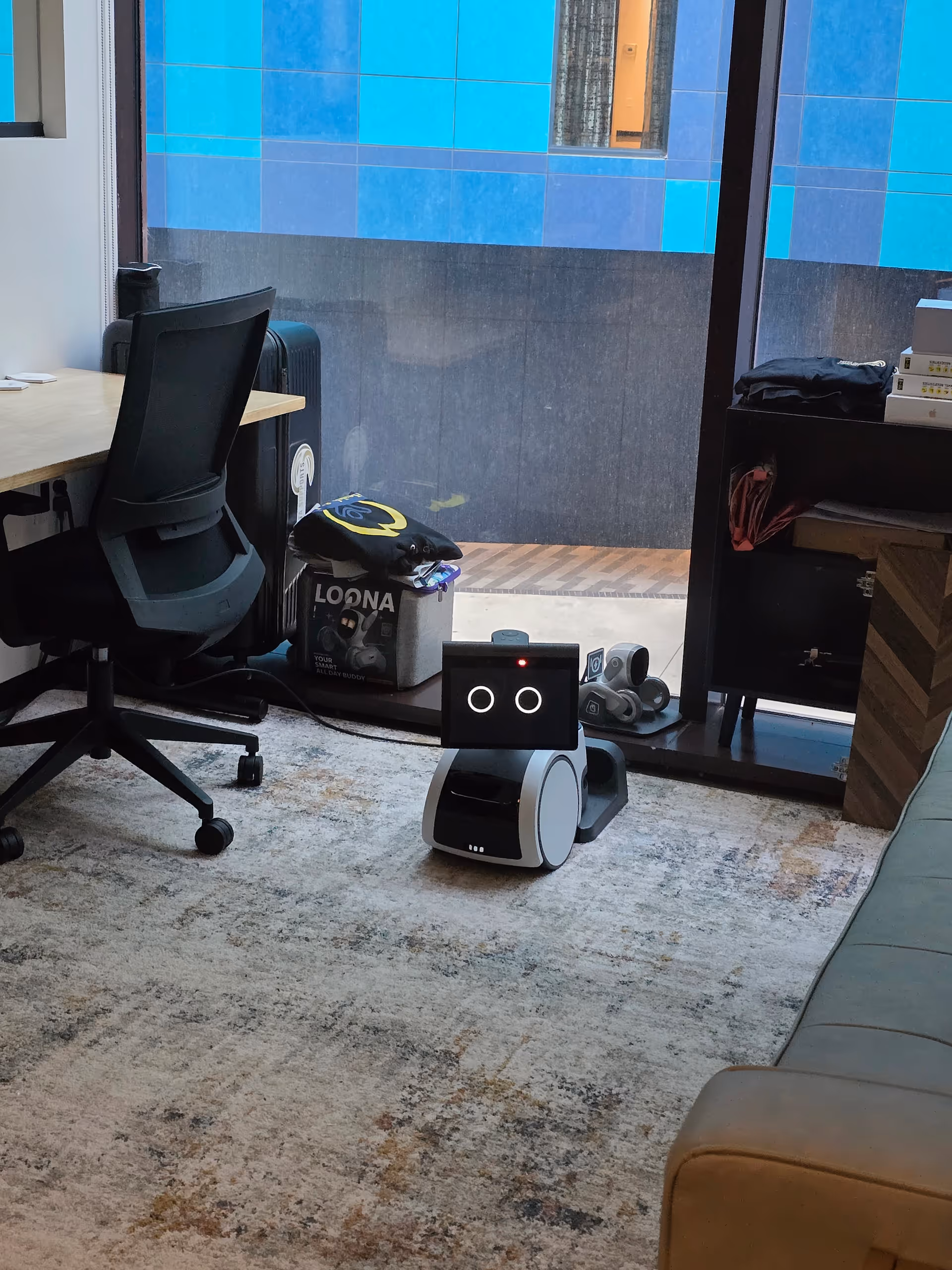 Small service robot with a screen and round eyes sits on the carpeted living room floor.