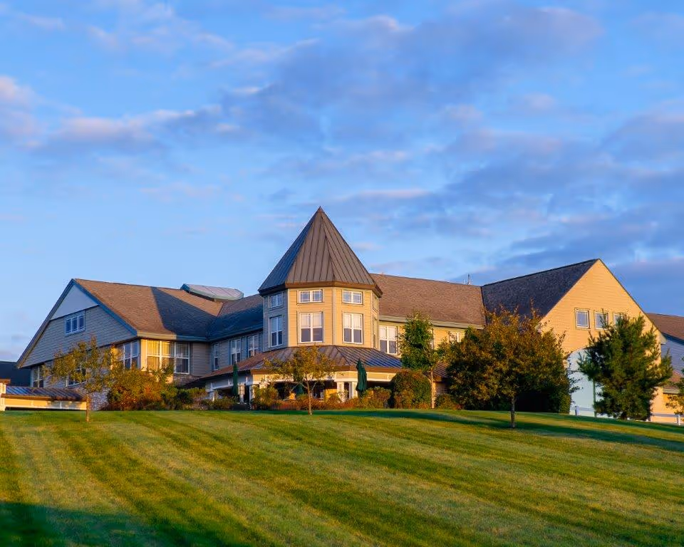Exterior view of a large senior living facility with a manicured lawn and blue sky.