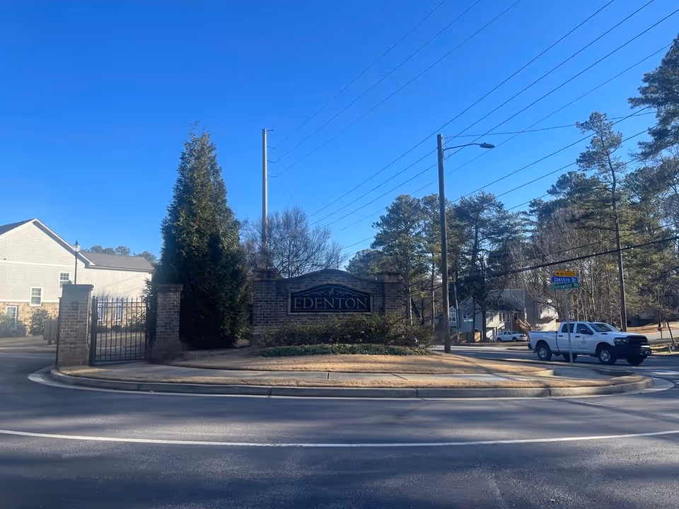 Brick gated entrance sign reading "EDENTON" at the front of a community beside a road with trees and a pickup truck.