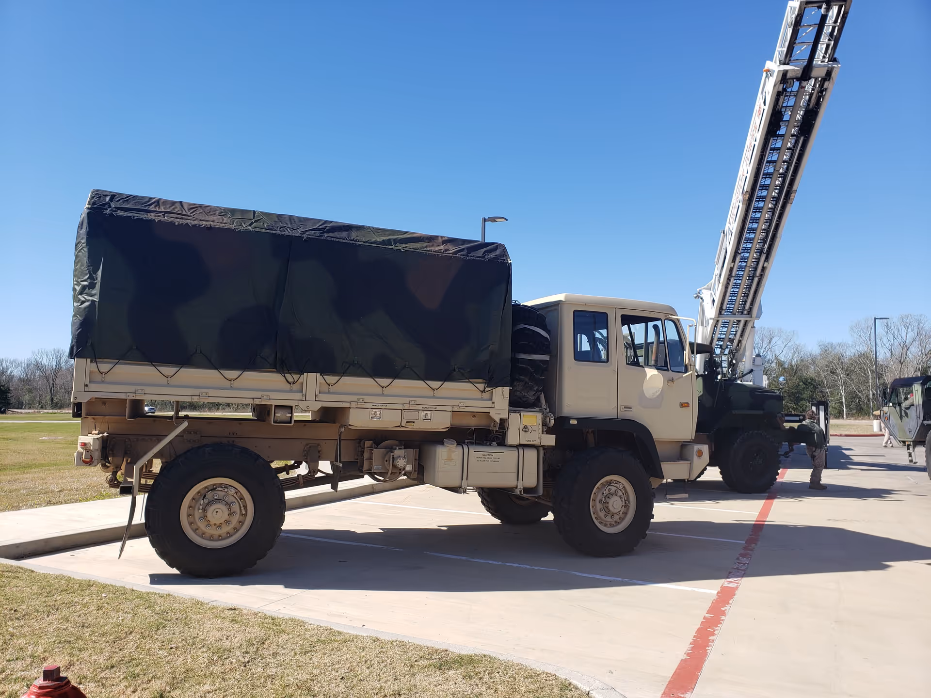 A large military-style truck with a covered cargo area parked in a sunny parking lot.