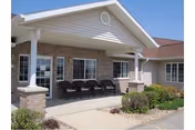 Front entrance of Wheatland Manor with a covered porch, brick exterior, and row of chairs.