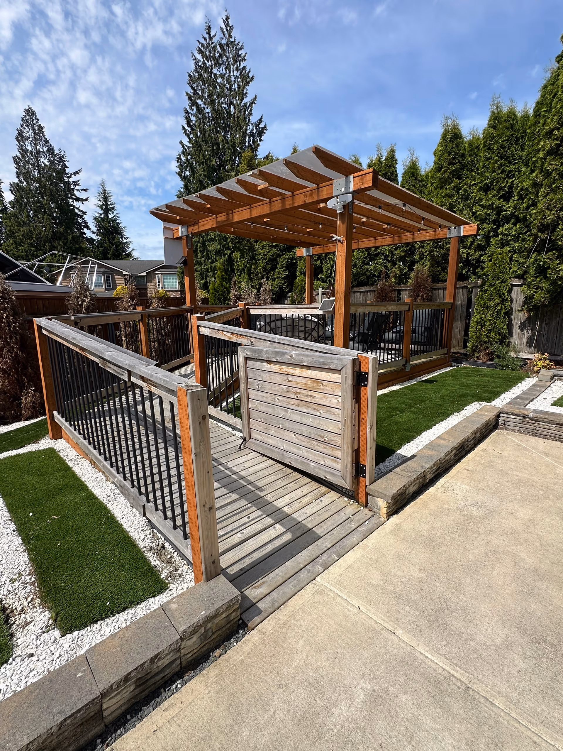 Outdoor wooden deck with a pergola, railing, and landscaped lawn area.