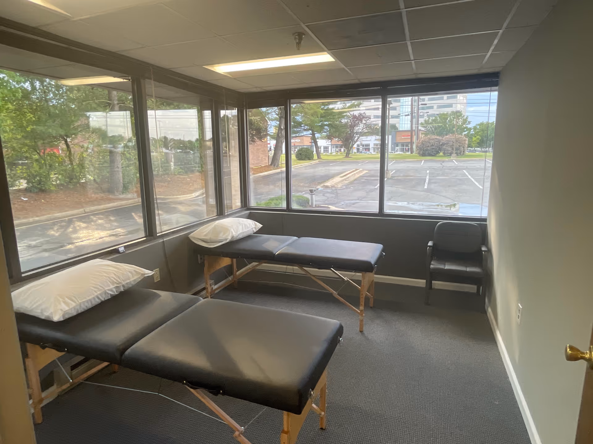 An interior room with two examination tables, pillows, and large windows overlooking parking.