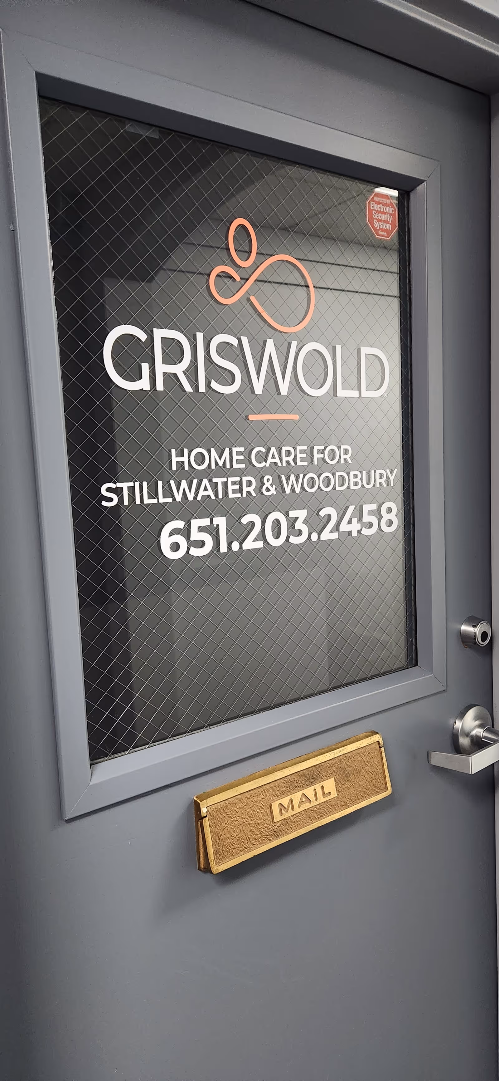Modern gray door featuring Griswold Home Care sign and a mail slot.
