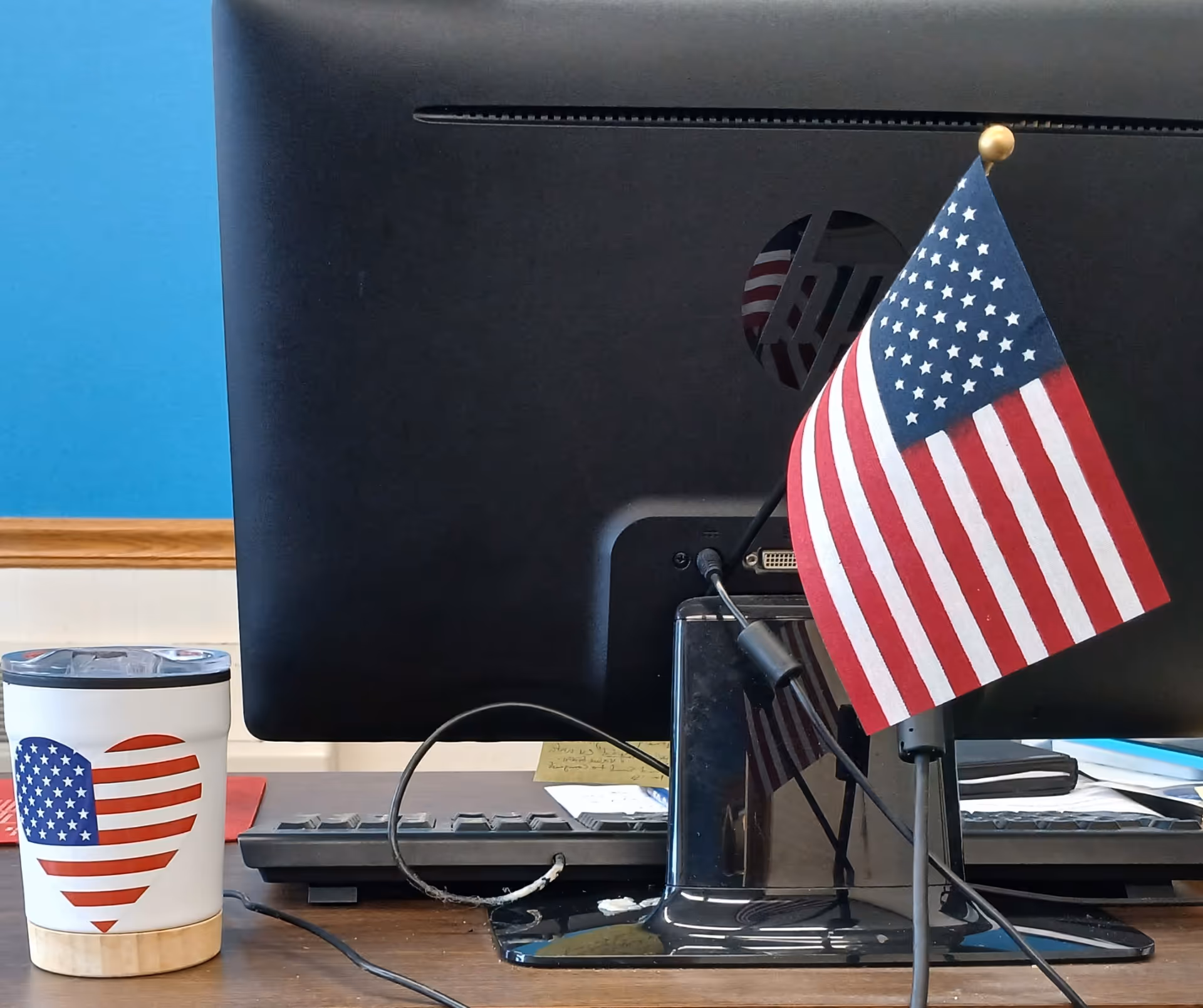 Desk with a computer monitor, American flag, and coffee cup on a wooden surface.