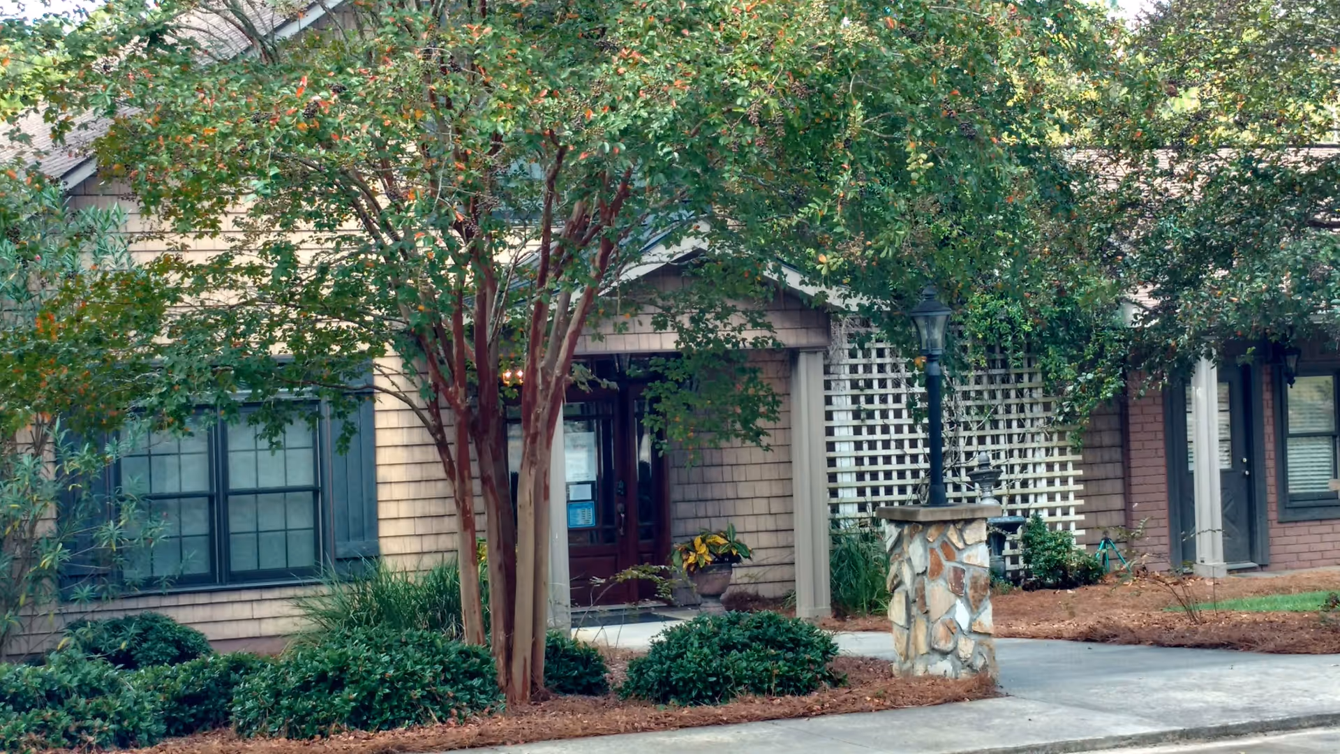 Exterior view of a senior living facility entrance with trees, shrubs, and a stone lamp.