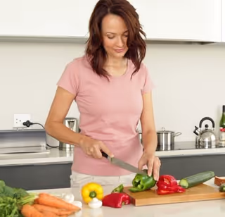 A woman in a pink shirt chops vegetables on a kitchen counter.