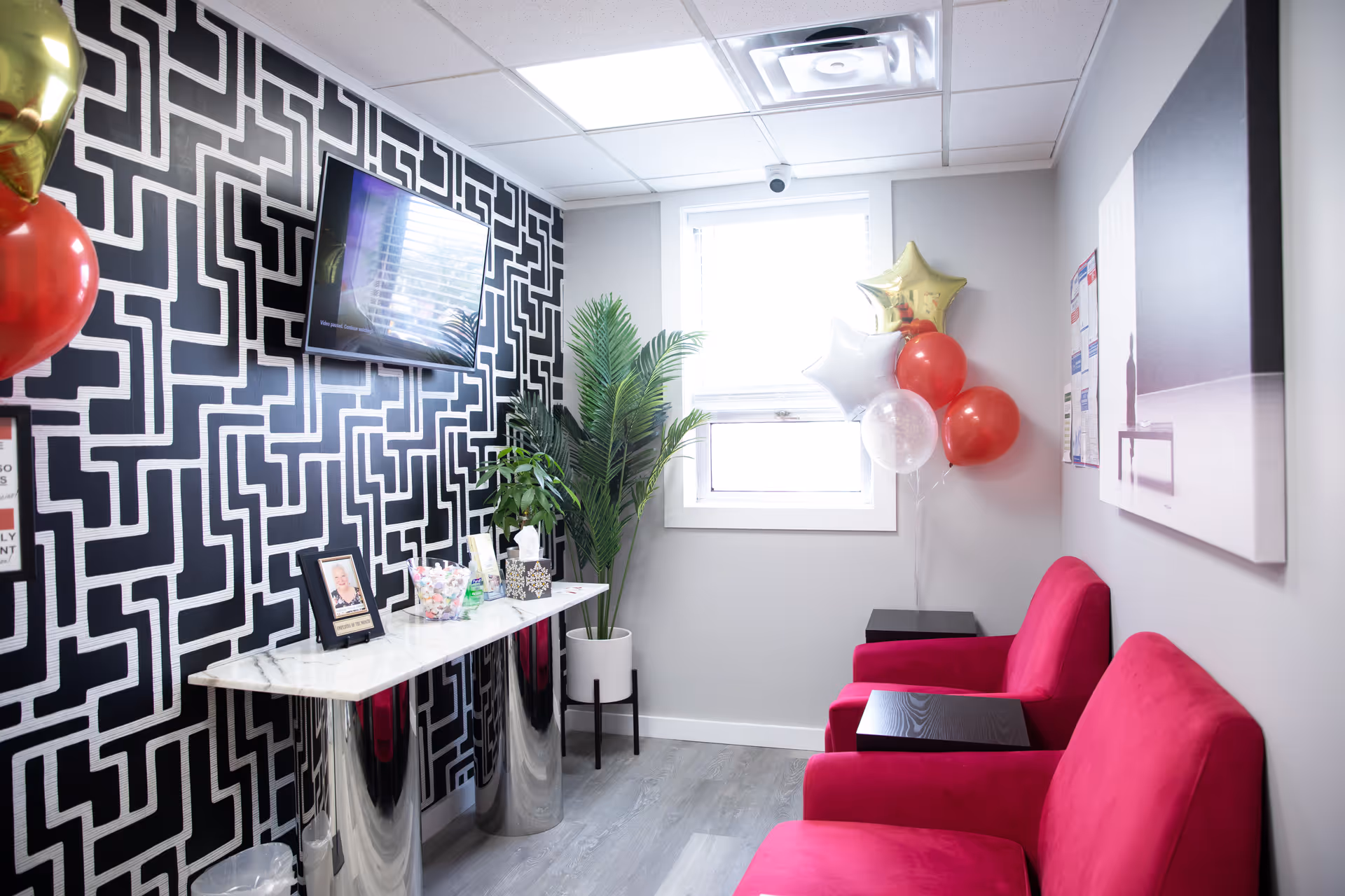 Lounge area with pink chairs, geometric wallpaper, balloons, TV, and a plant.