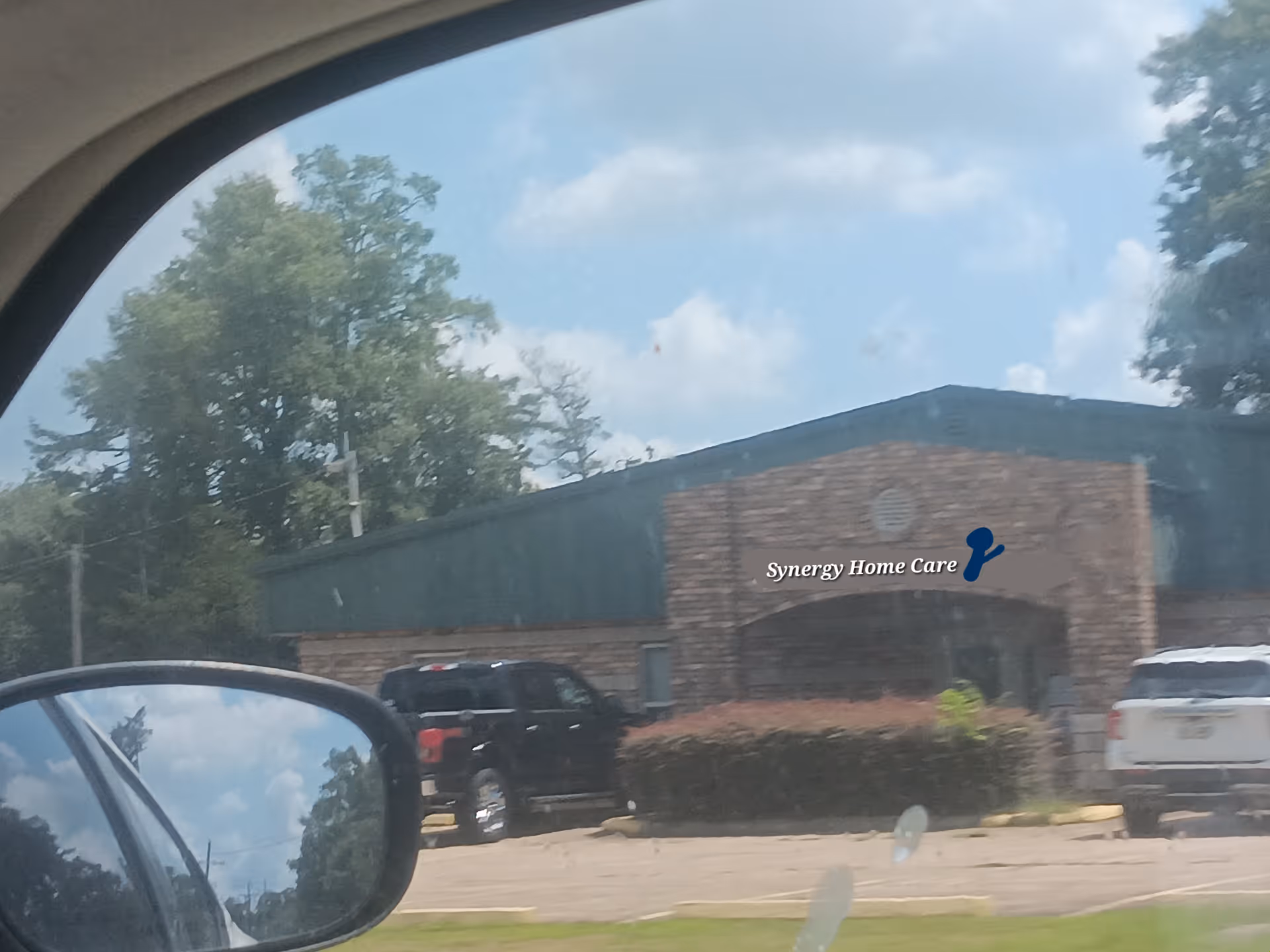 Exterior view of a brick building with Synergy Home Care signage and parking.