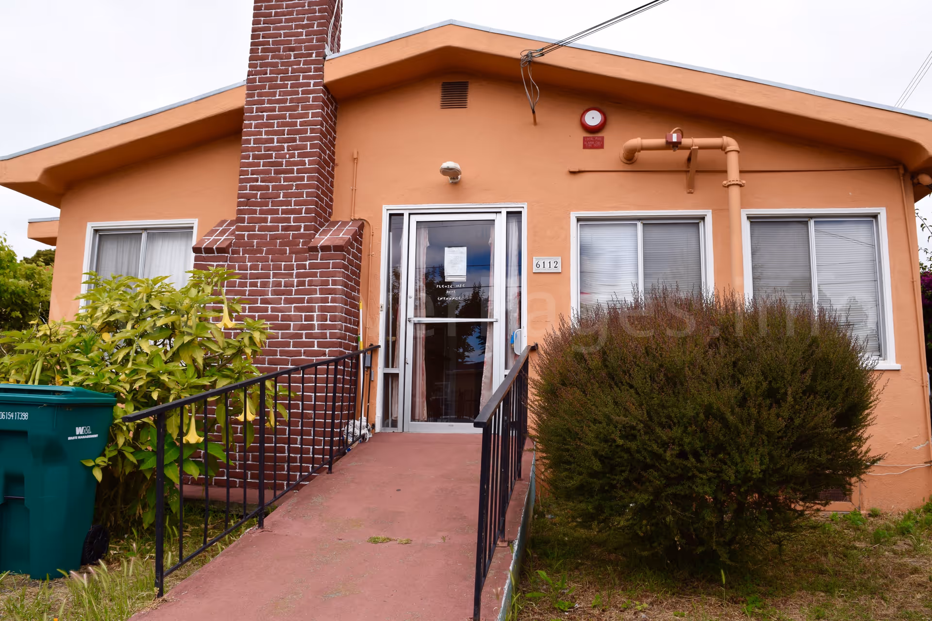 Orange single-story facility entrance with ramp, brick chimney, and shrubs outside.