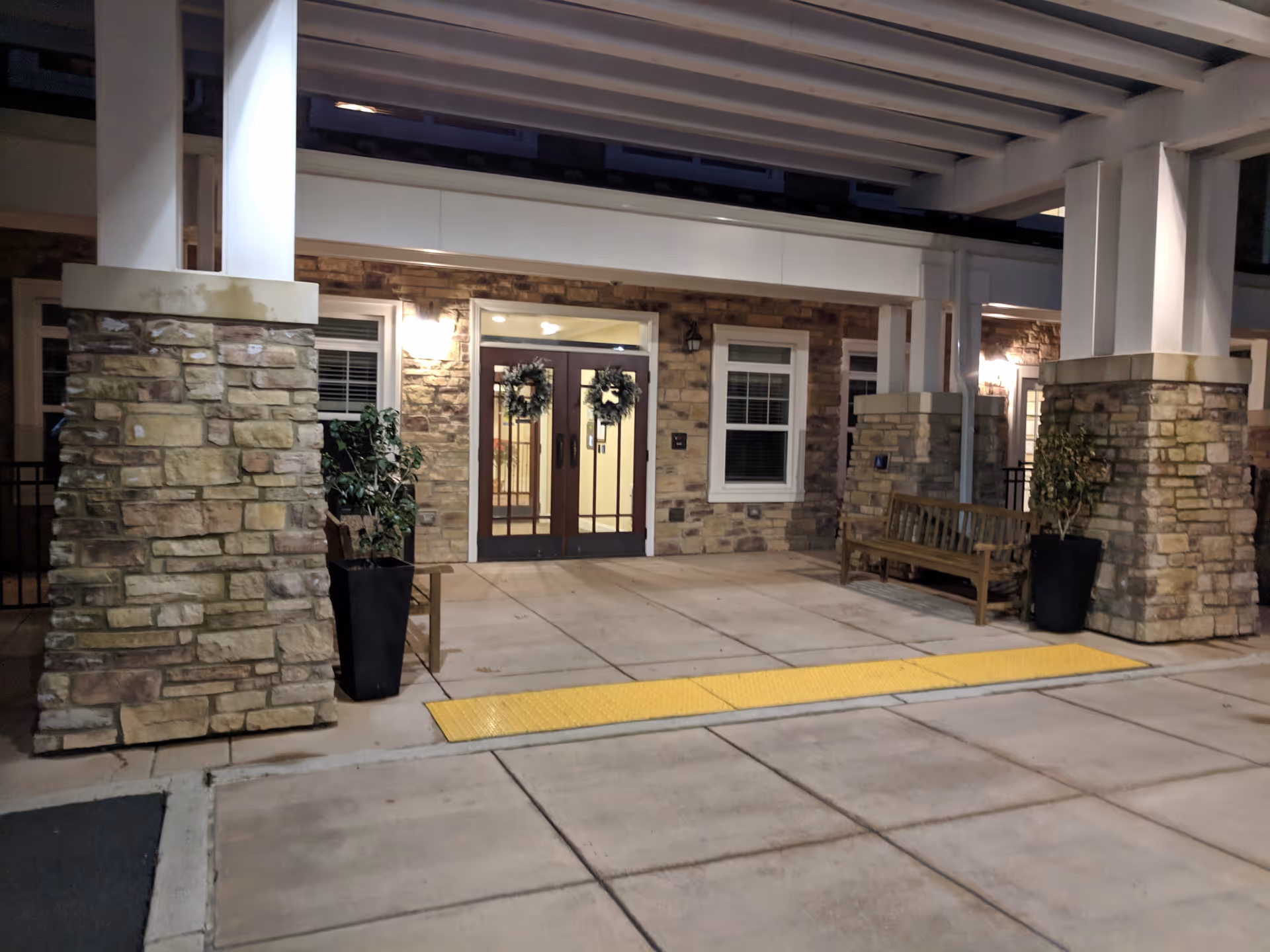 Exterior view of Brightview Great Falls entrance with stone pillars and wooden bench.