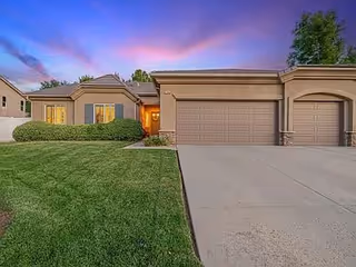 Single-story facility exterior with a double garage, manicured lawn, and sunset sky.