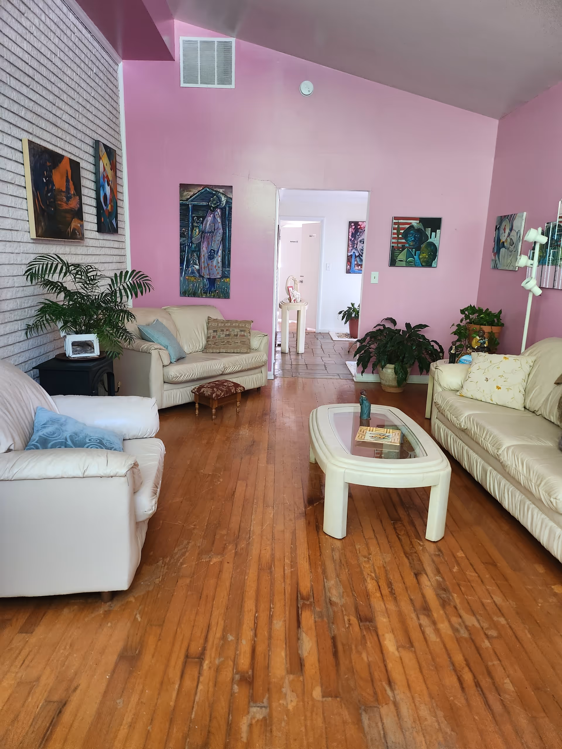 Bright pink-walled living room with beige sofas, artwork, and a glass coffee table.