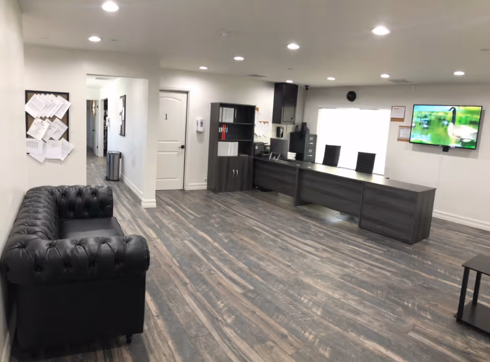 A modern reception desk, black tufted sofa, hallway, and mounted TV in a spacious lobby.