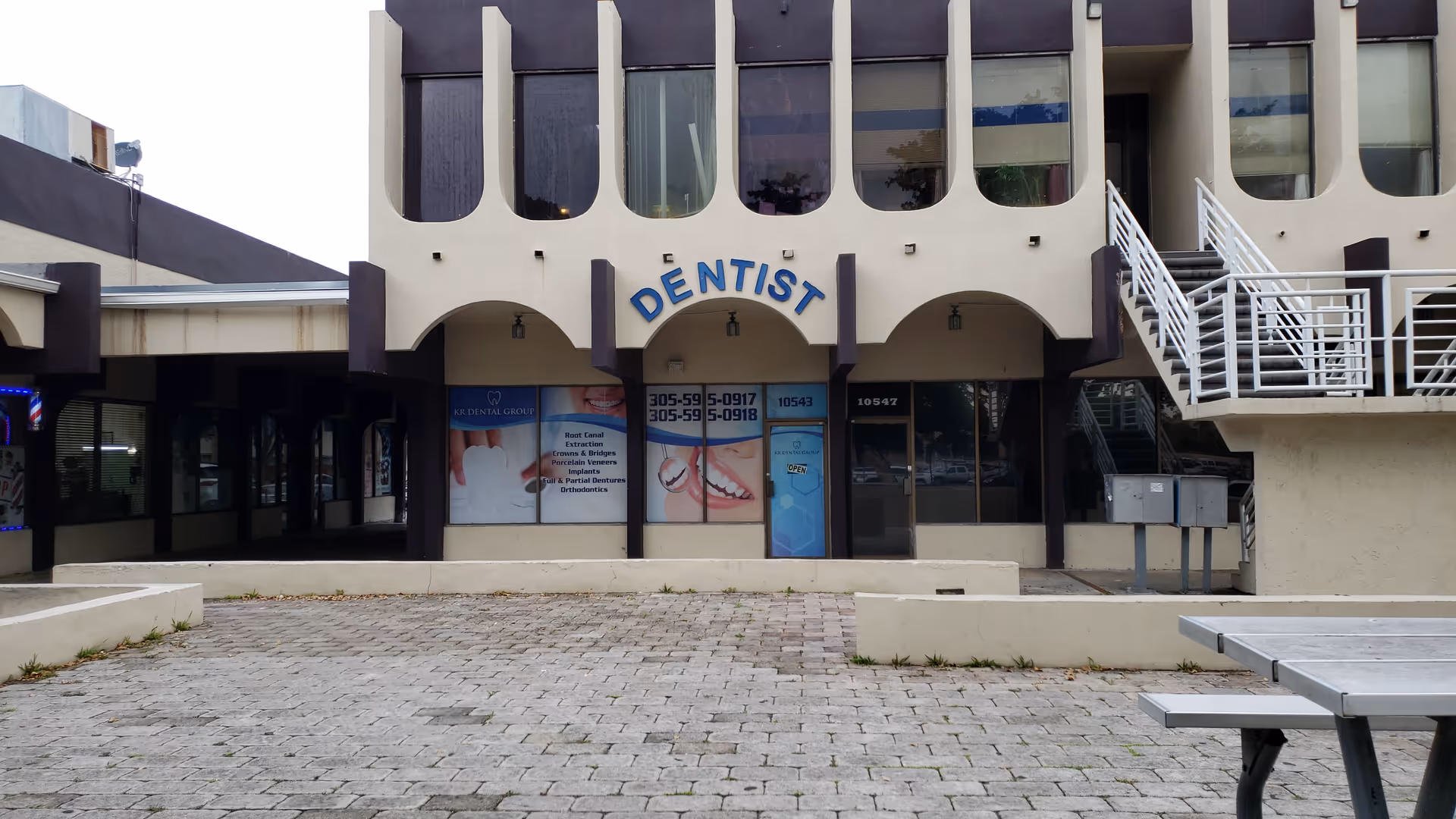 Facade of a building with a dentist sign, arches, stairs, and a paved courtyard.