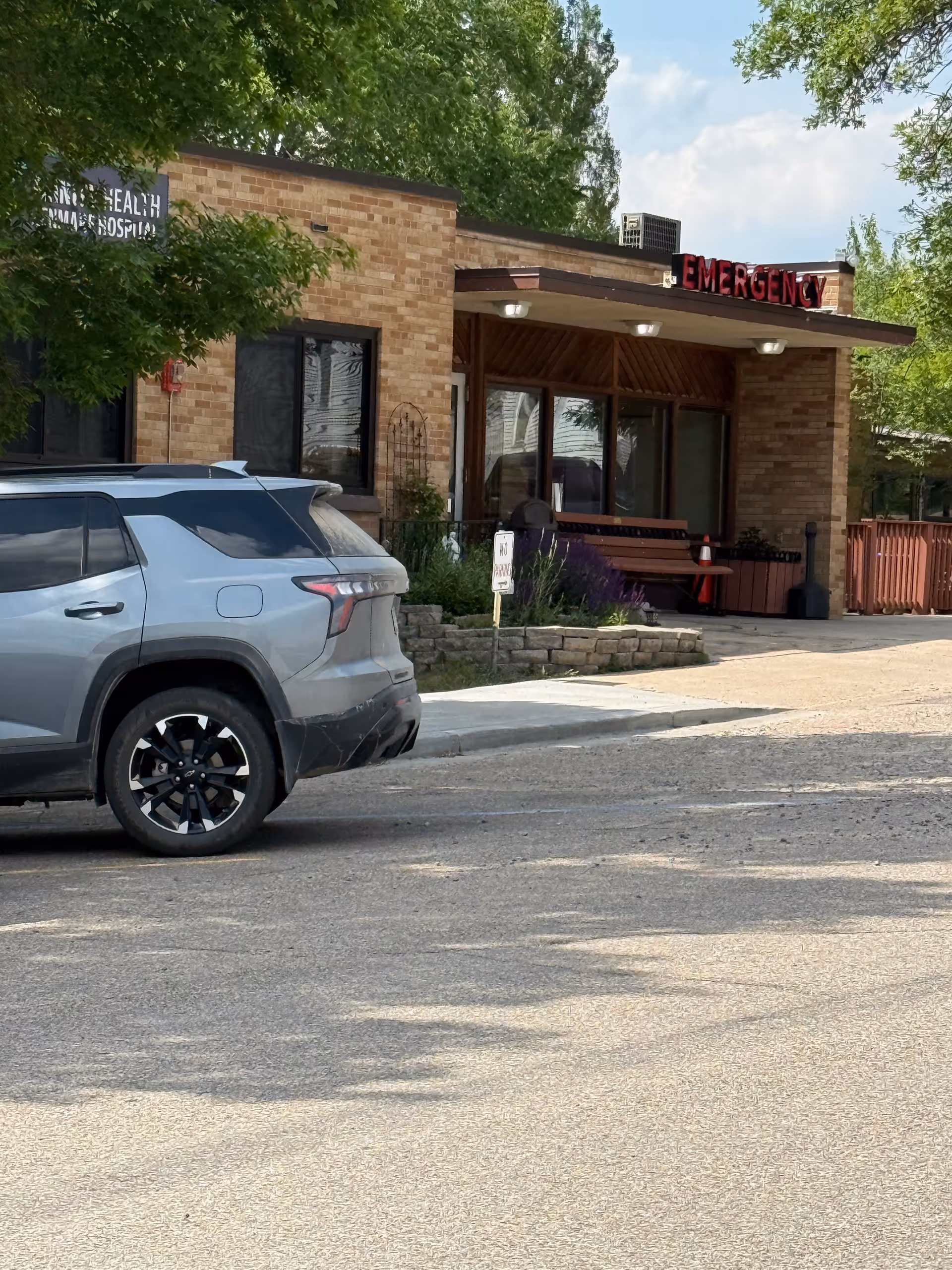 Brick hospital exterior with emergency entrance and a parked SUV in front