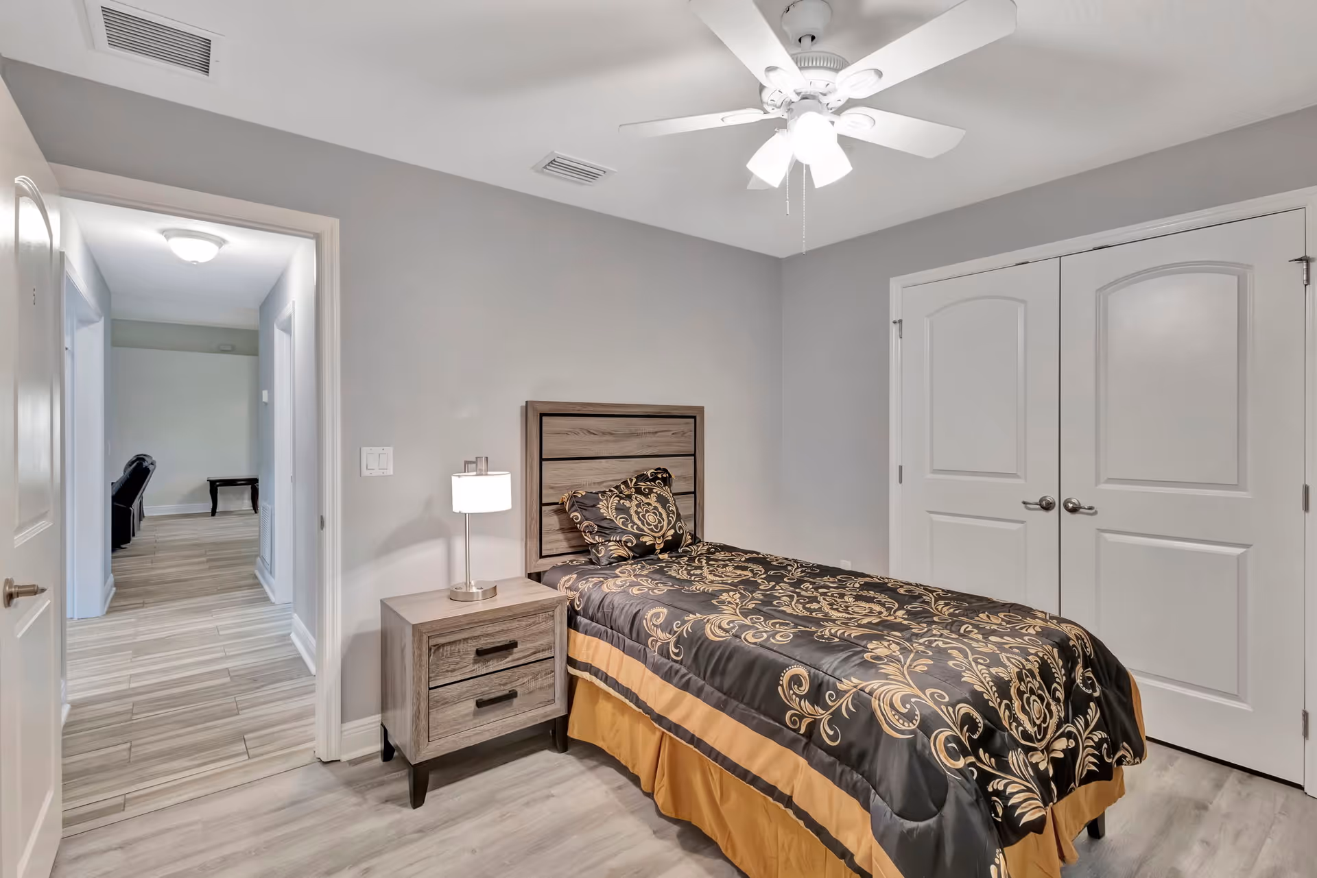 Cozy bedroom with bed, nightstand, lamp, ceiling fan, and double closet doors.