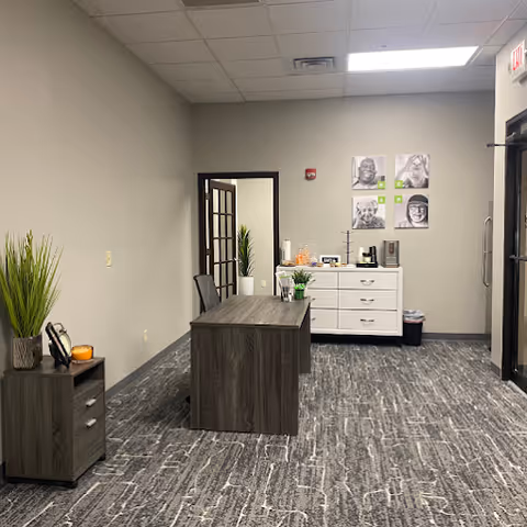 Reception area with desk, cabinets, plants, and wall art in a neutral office.