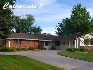 Single-story brick senior living facility with curved driveway, manicured lawn, and mature trees.