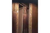 Narrow bathroom with mosaic-tiled doorway and hanging shower curtains.