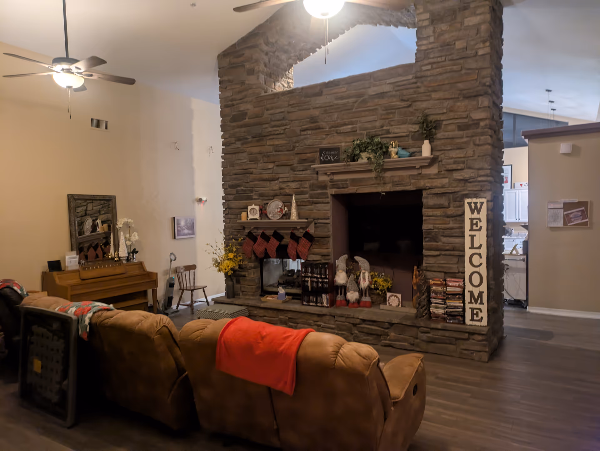 Cozy living room with stone fireplace, fans, and couch seating in a senior home.