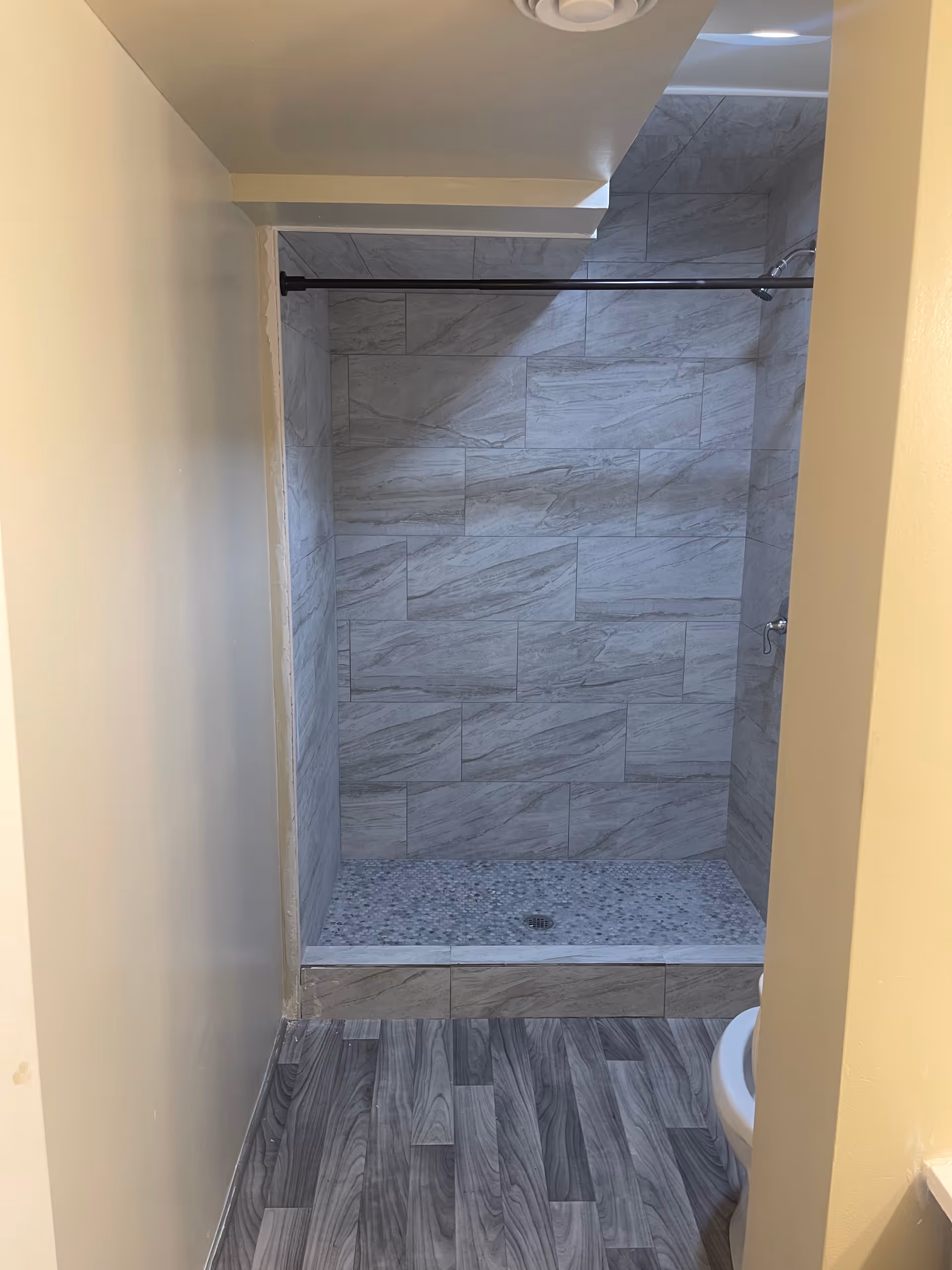Walk-in shower with gray marble tile walls, pebble floor, and a visible toilet edge.
