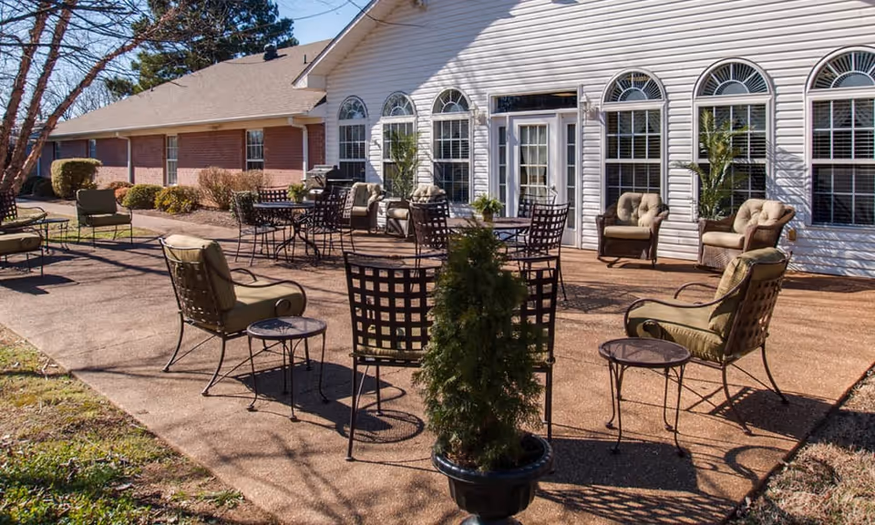 Outdoor patio with chairs, tables, and potted plants in front of a RiverWick building with arched windows.