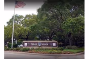 Front brick sign reading Mease Manor with flag and trees nearby.