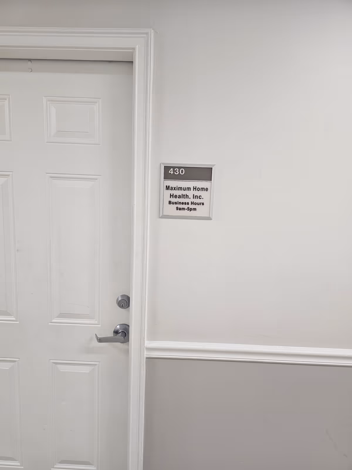 White interior hallway with a closed paneled door and a wall sign reading 430.