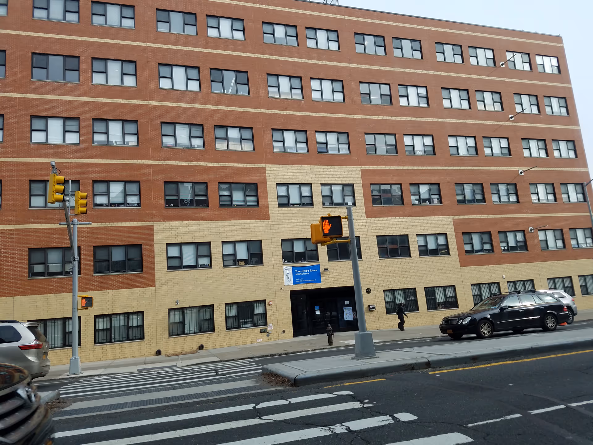 Front view of a brick multi-story building with windows and street crossing.