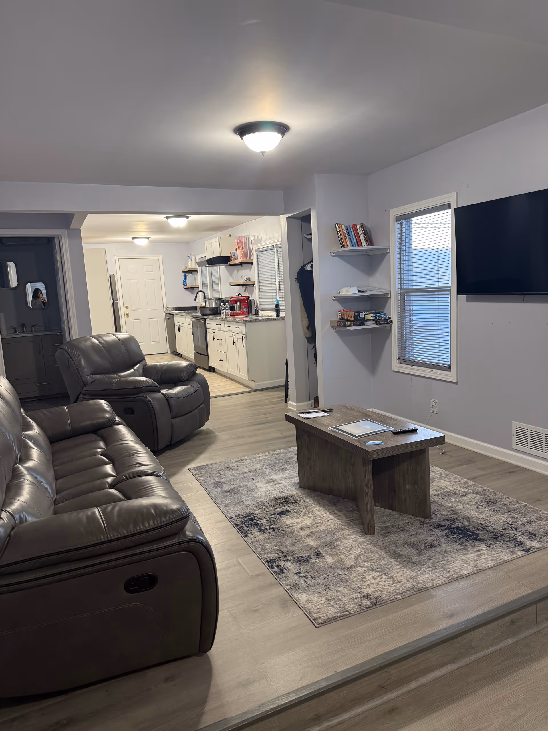 Cozy living room with leather sofas, a coffee table, rug, and open kitchen.