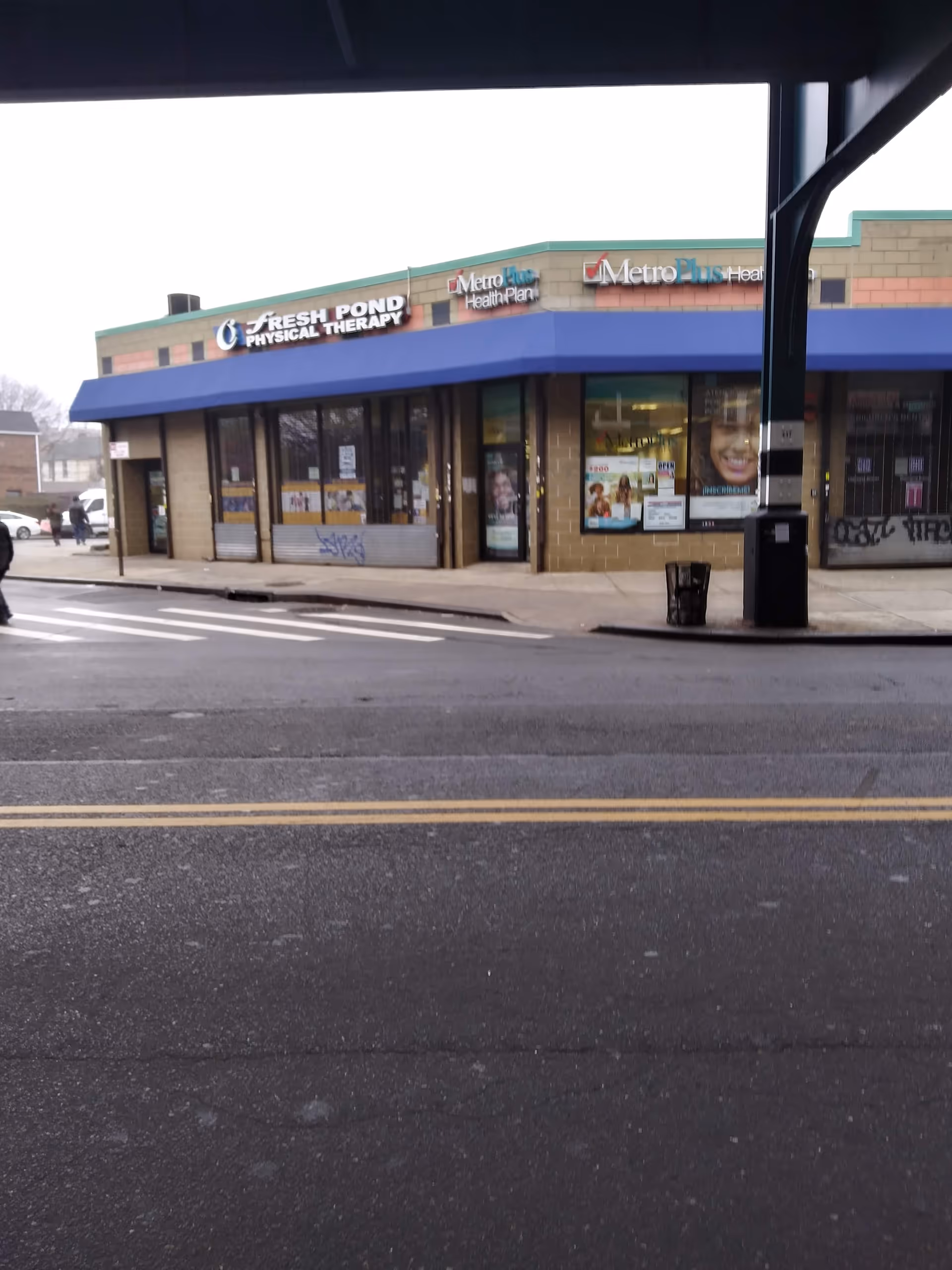 Street-level view of a strip mall storefront with blue awning and multiple signs.