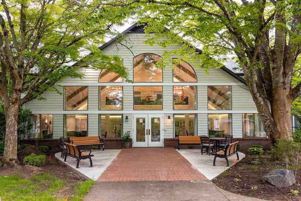 Santiam Gardens exterior with glass entrance and benches among trees.