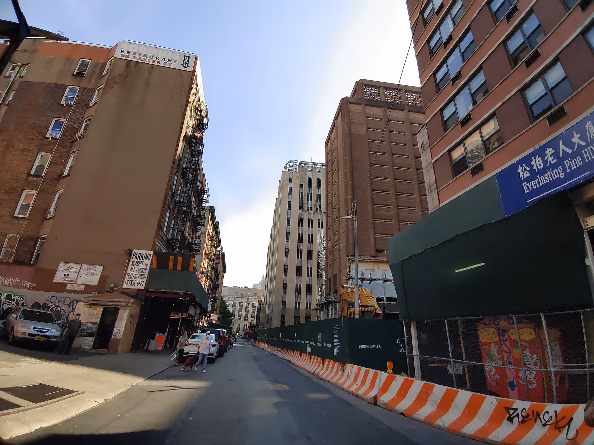 Exterior city street with tall buildings, orange construction barriers, and a blue Everlasting Pine HDFC sign.