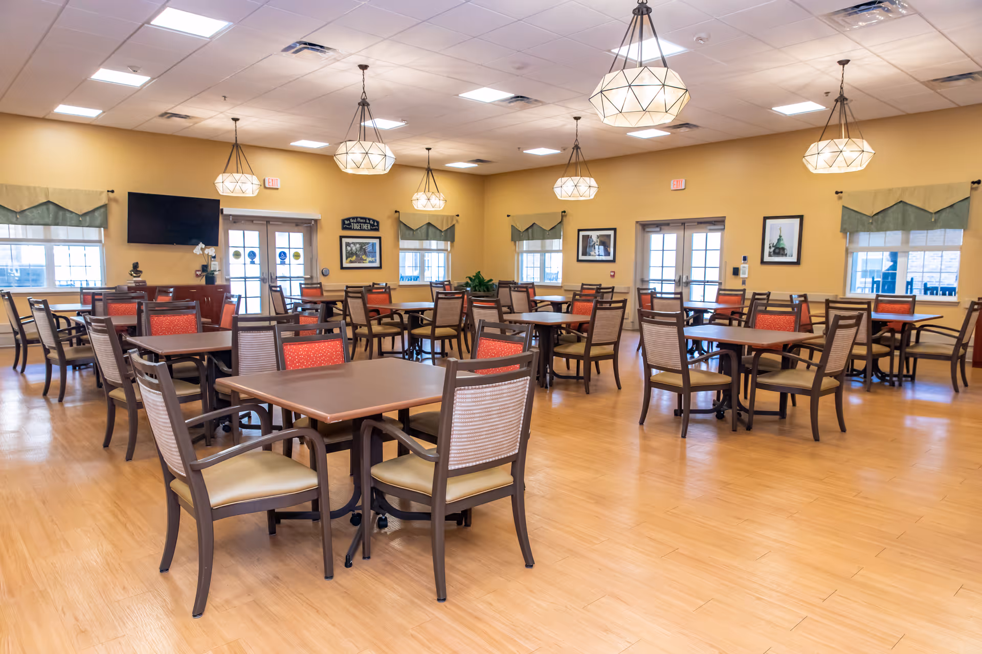 Spacious dining room with multiple tables and chairs, pendant lights, windows, and double doors.