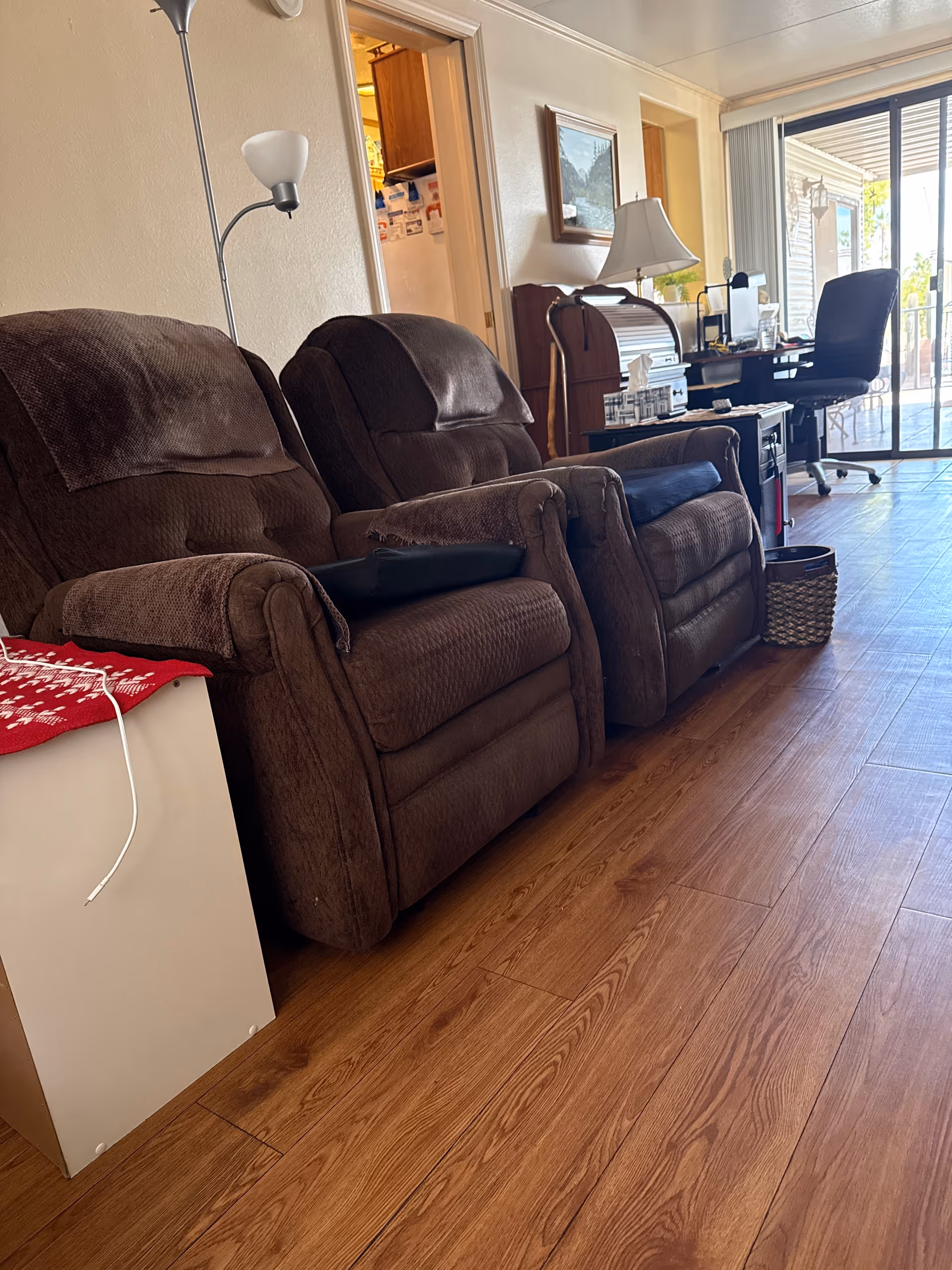 Cozy senior living lounge with brown recliners, a desk, lamp, and glass door.