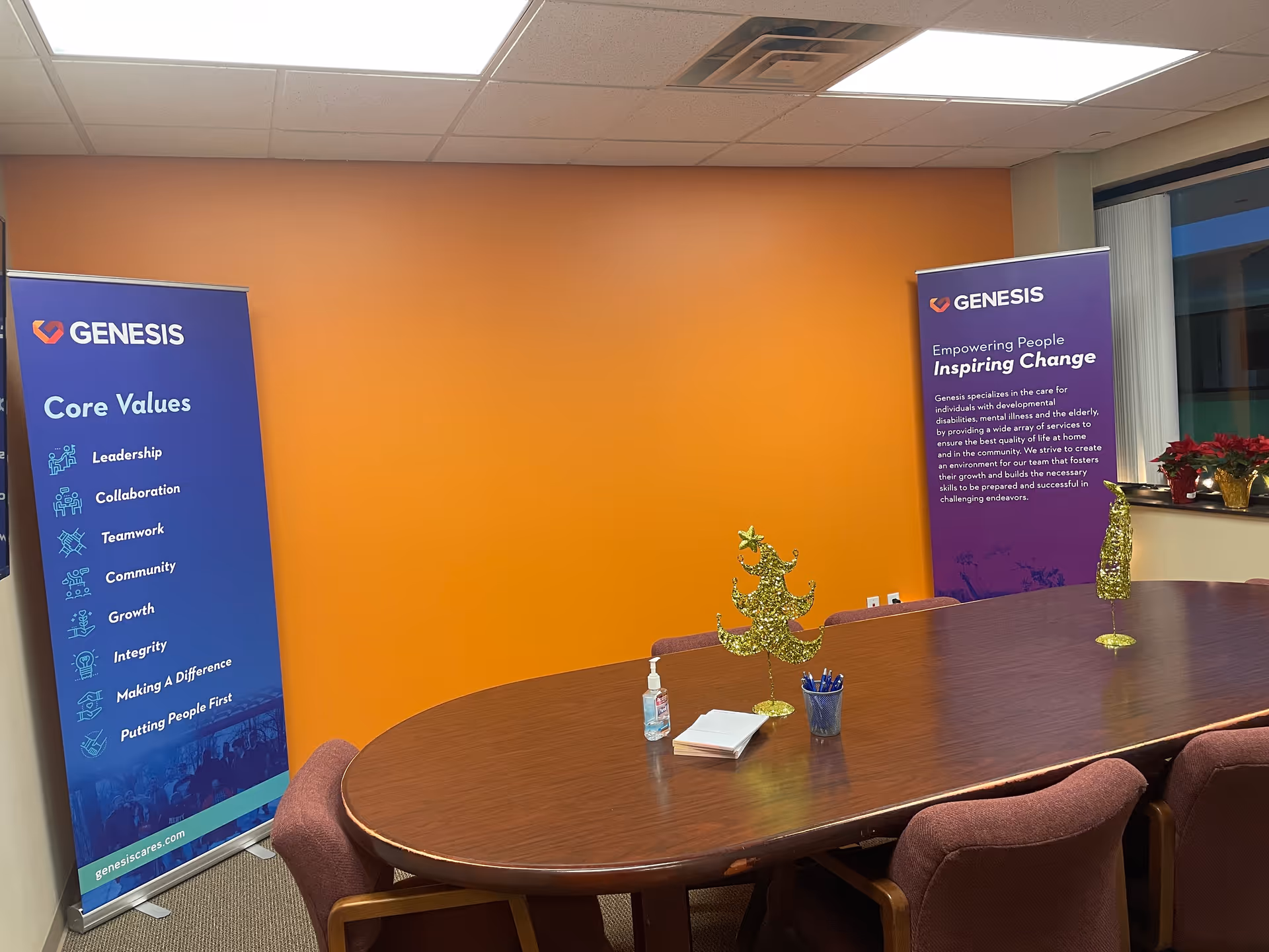 Orange wall backdrop with round table and Genesis banners in a meeting room.