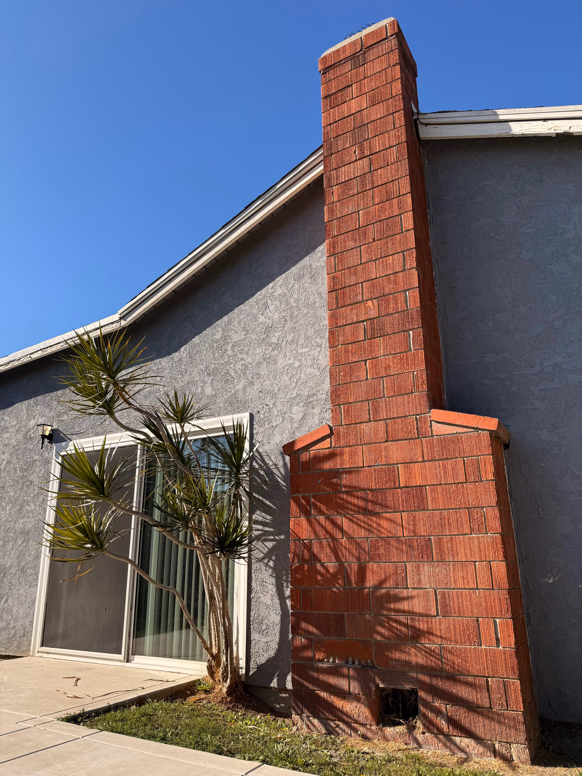 Gray senior living building exterior with a tall red brick chimney beside a sliding glass door.
