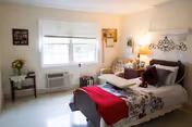 A bright, neatly arranged bedroom with a bed, window, nightstands, and decorative wall accents.