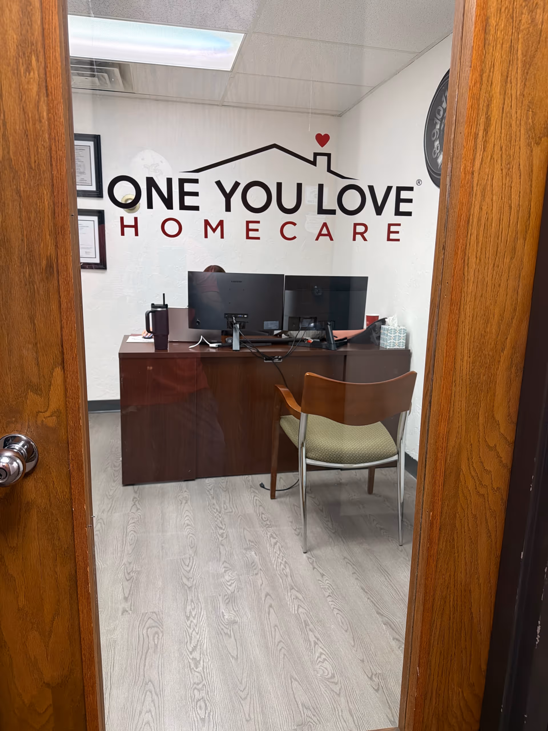 Reception desk with dual monitors in office bearing One You Love Homecare logo.
