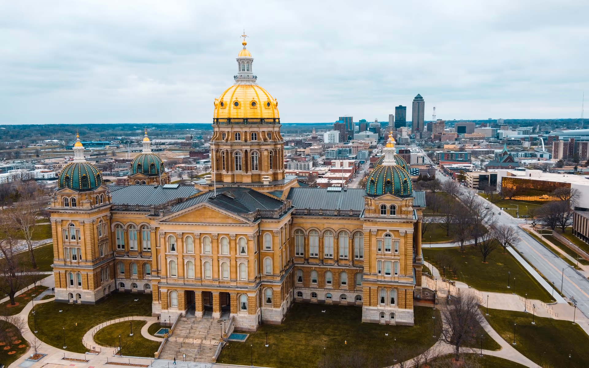 Aerial view of a grand historic building with a gold central dome and city skyline.