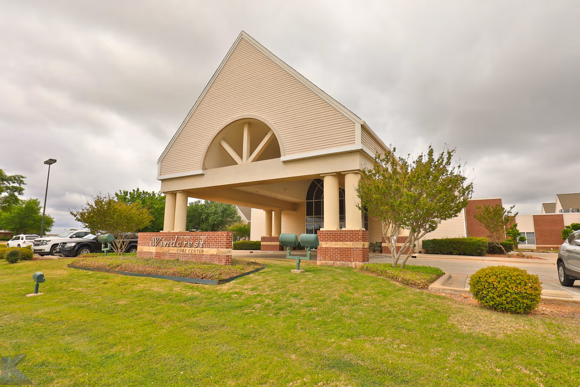Exterior view of a senior living facility entrance with arches, columns, and a manicured lawn.