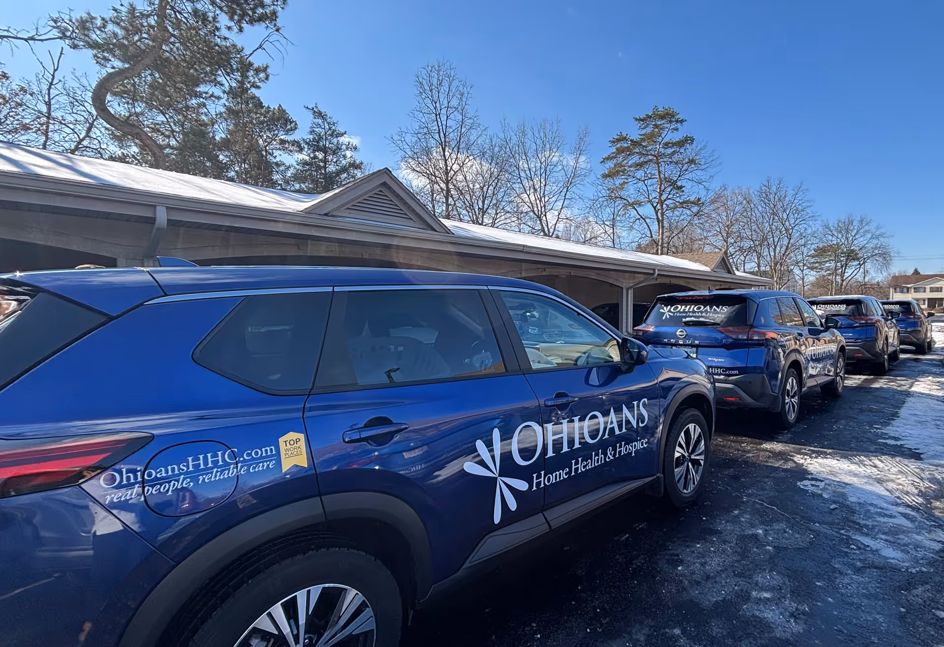 Blue branded SUVs for Ohioans Home Health & Hospice parked outside a building.