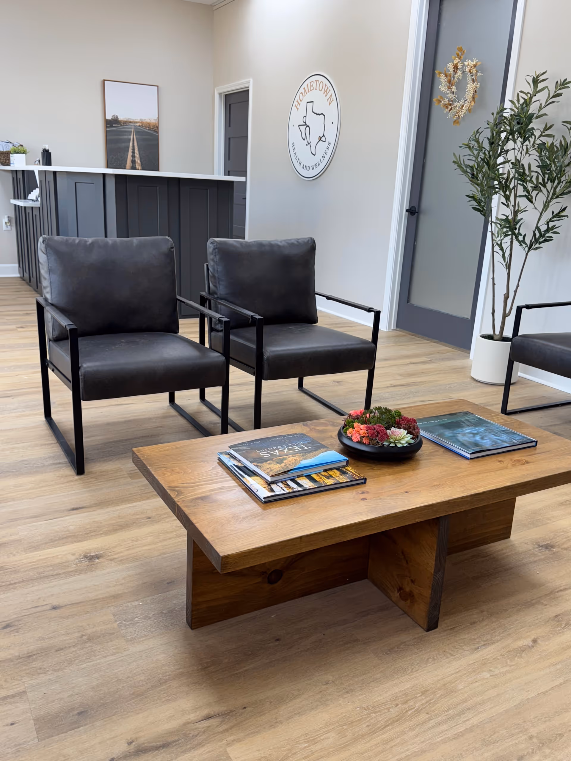 Modern lobby reception area with two black chairs, wooden coffee table, magazines, and a plant.