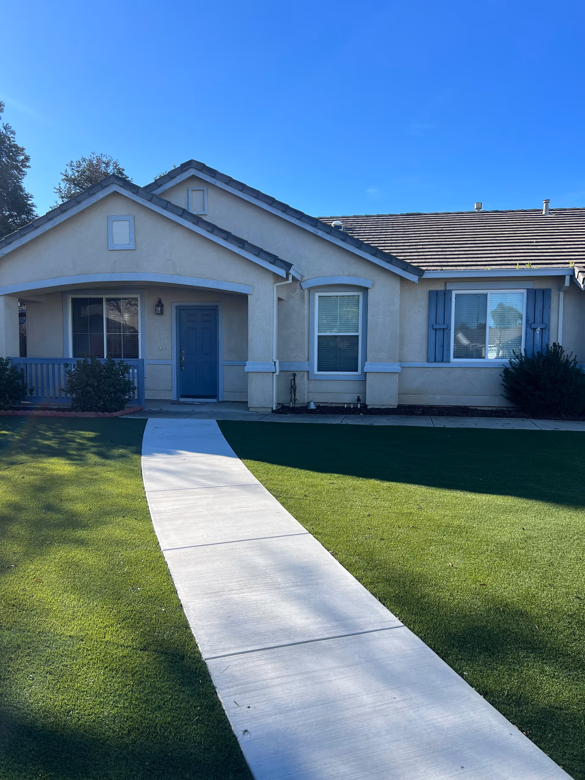 A single-story beige building with blue trim, a curved concrete walkway, and green lawn.