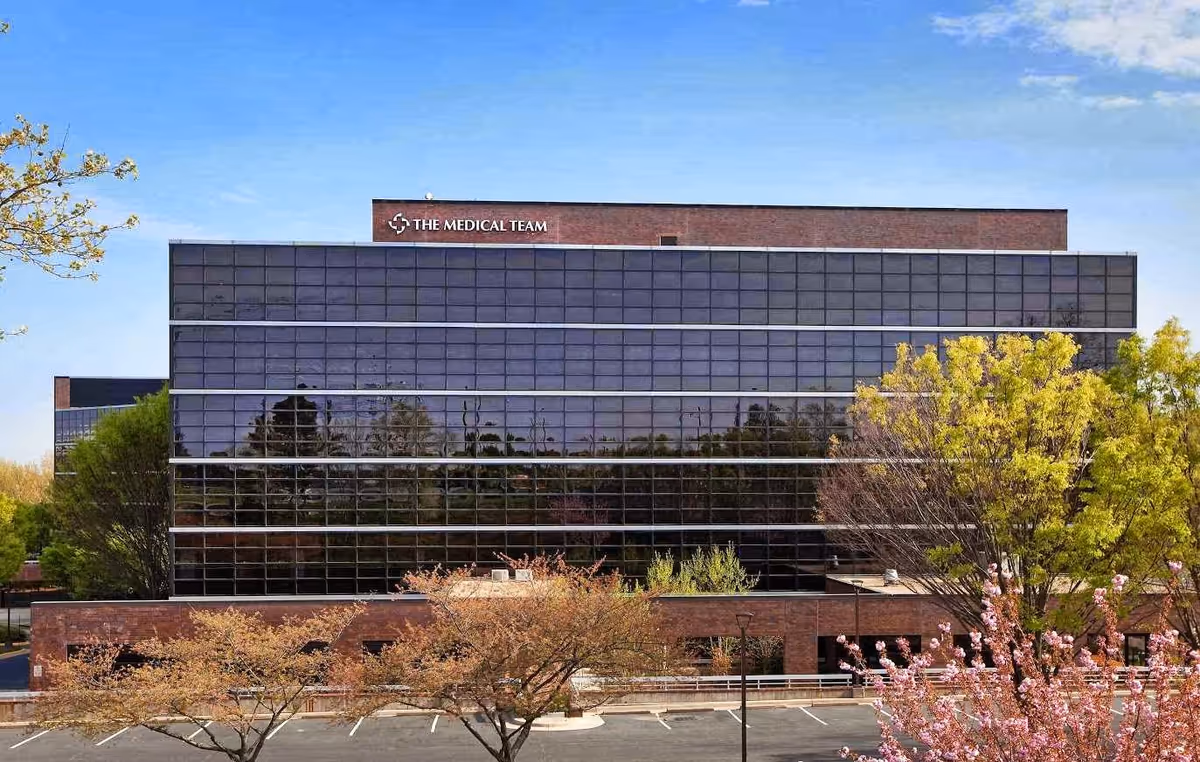 Modern glass-front medical building with trees and a sign reading The Medical Team