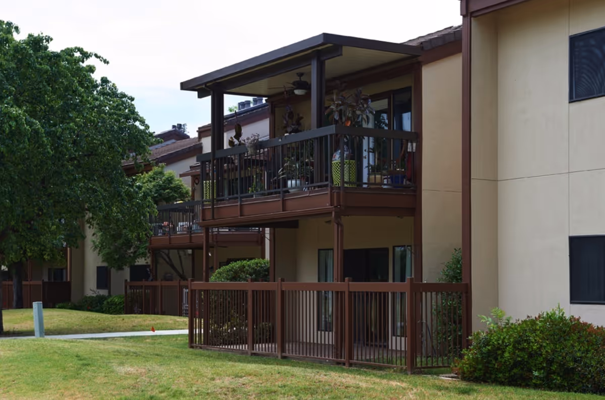 Exterior view of a multi-unit senior living building with fenced ground-floor patios and covered second-story balconies.