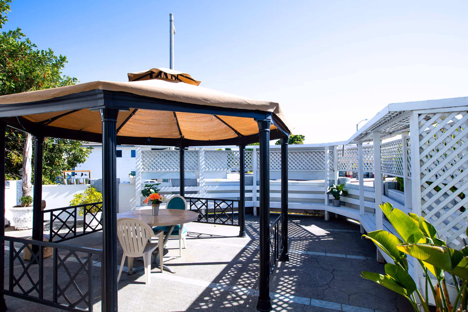 Outdoor shaded patio with a gazebo, table and chairs, lattice fencing and potted plants.