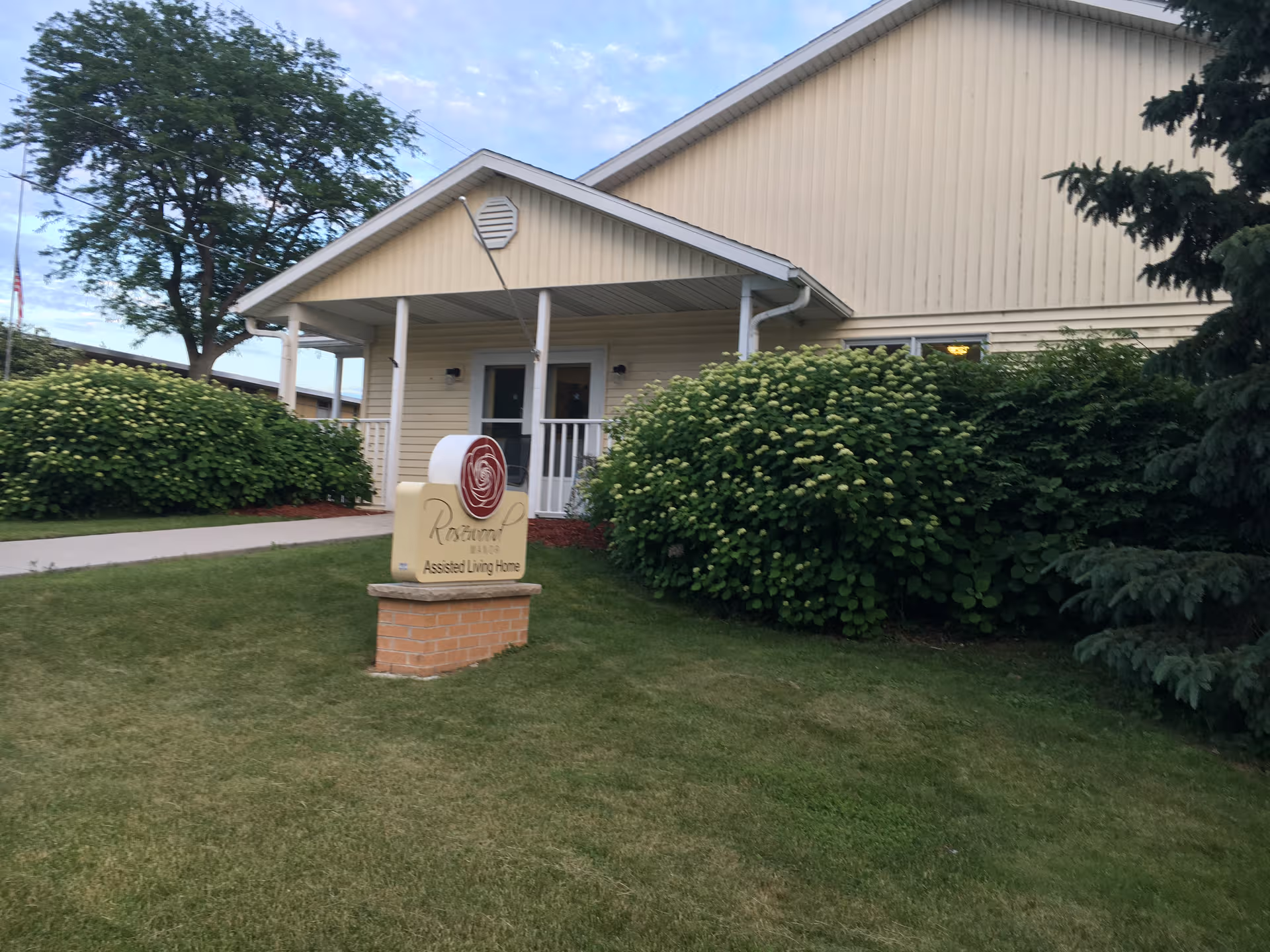 Front view of Rosewood Manor assisted living home with sign and shrubs
